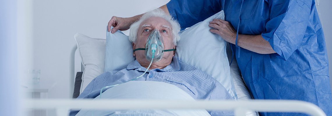 Male patient wearing an oxygen mask being propped up in bed.
