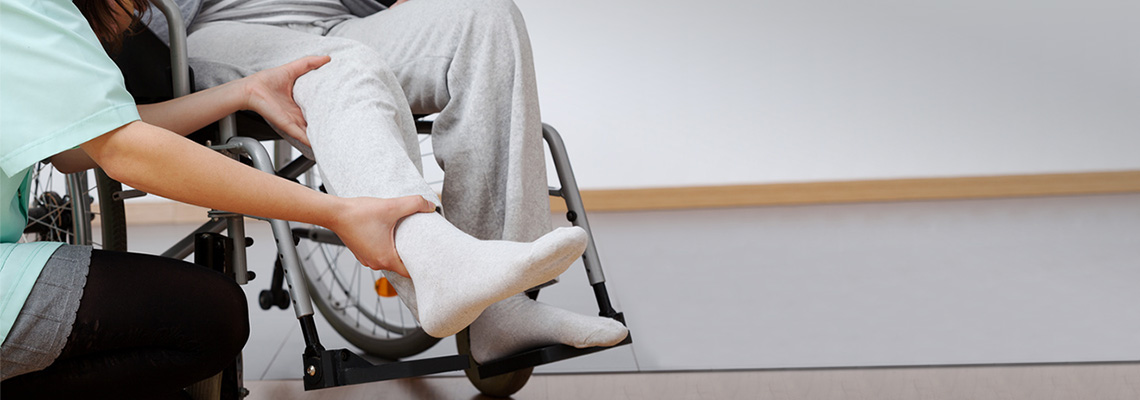 Therapist examining a patient's lower leg while they are sitting in a wheelchair.