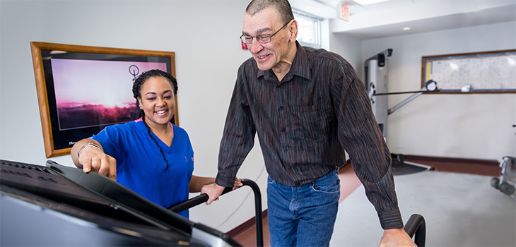 Resident smiling while using the treadmill and working with a therapist