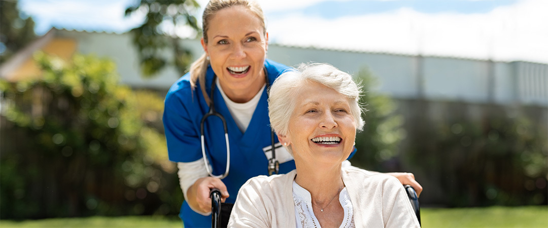 A senior in a wheelchair and a nurse outside on a walk together.