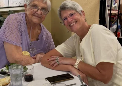 Two senior women sit together at a table, enjoying food and drinks.