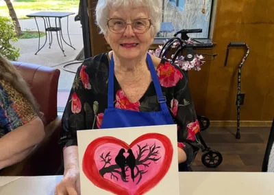 A resident shows off a Valentine's Day card she painted of two birds sitting on a branch, surrounded by a heart.