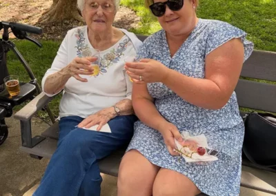 A resident sits outside with a family member, clinking glasses of a beverage together.
