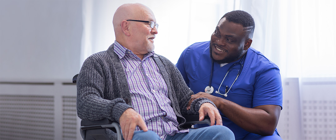 A nurse smiling with an elderly man in a wheelchair