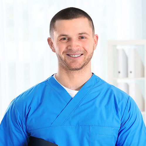 A smiling nurse in scrubs holding a folder under his arm.