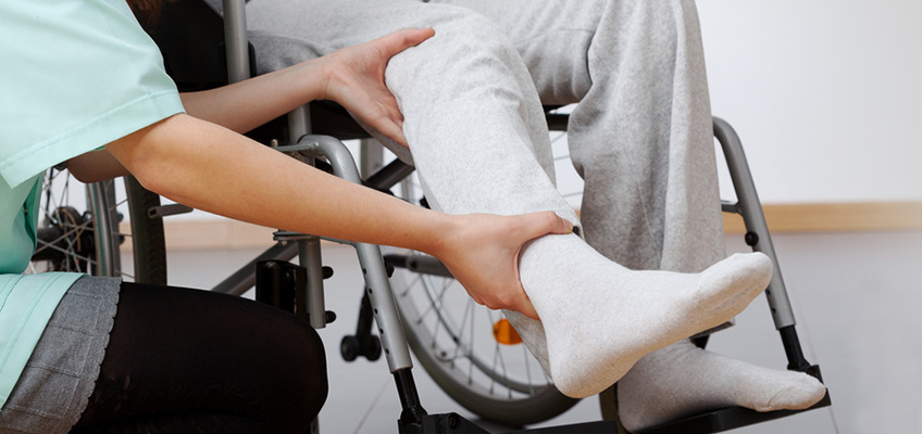 Healthcare worker helping person's leg into a wheelchair.