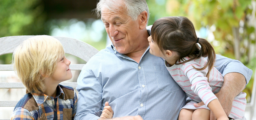 Senior man outside with two young children on his lap.