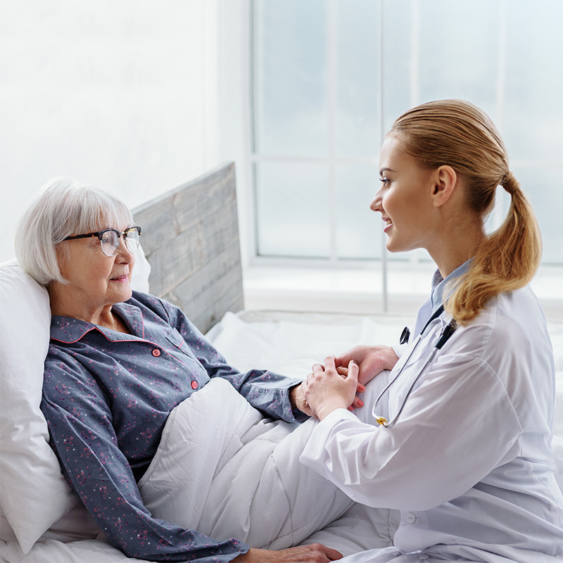 Medical Director in white lab coat hohlding hand of senior woman in bed.
