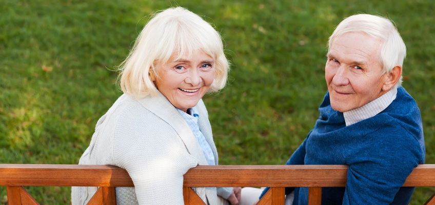 Woman and a man smiling seated on a bench outdoors on a nice day