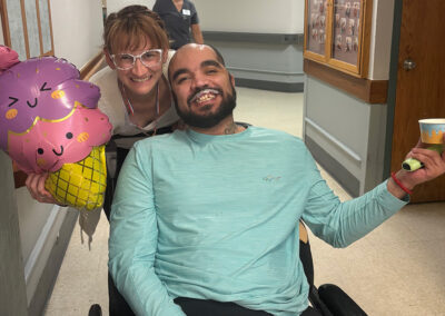 A resident smiling with a cup of ice cream next to a nurse holding a balloon at Lowry Hills