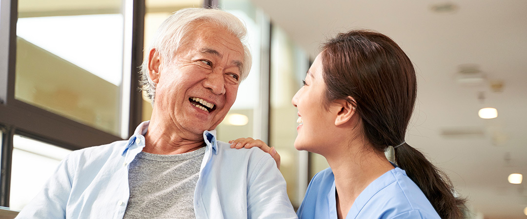 A nurse kneeling down beside a senior man smiling up at him. A nurse kneeling down beside a senior man smiling up at him.