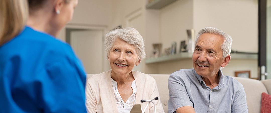 A senior couple sitting on a couch and speaking with a nurse. A senior couple sitting on a couch and speaking with a nurse.
