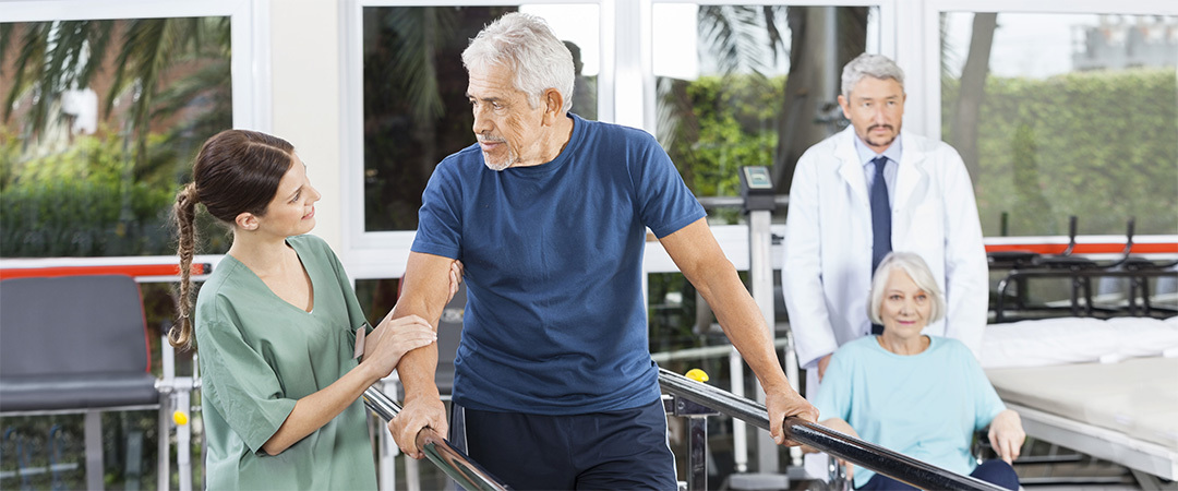 Two seniors outside in a rehabilitation room working on parallel bars with rehabilitation professionals. Two seniors outside in a rehabilitation room working on parallel bars with rehabilitation professionals.