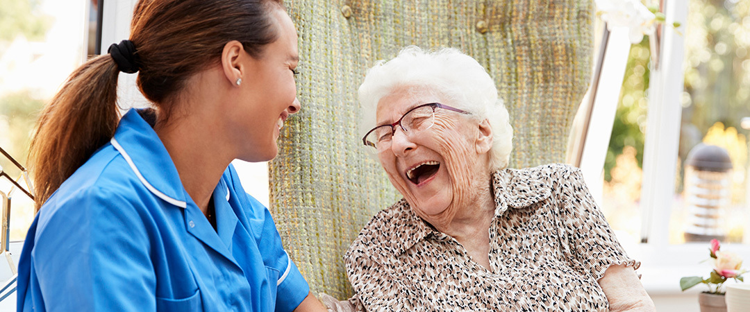 A senior woman laughing outside beside her nurse.