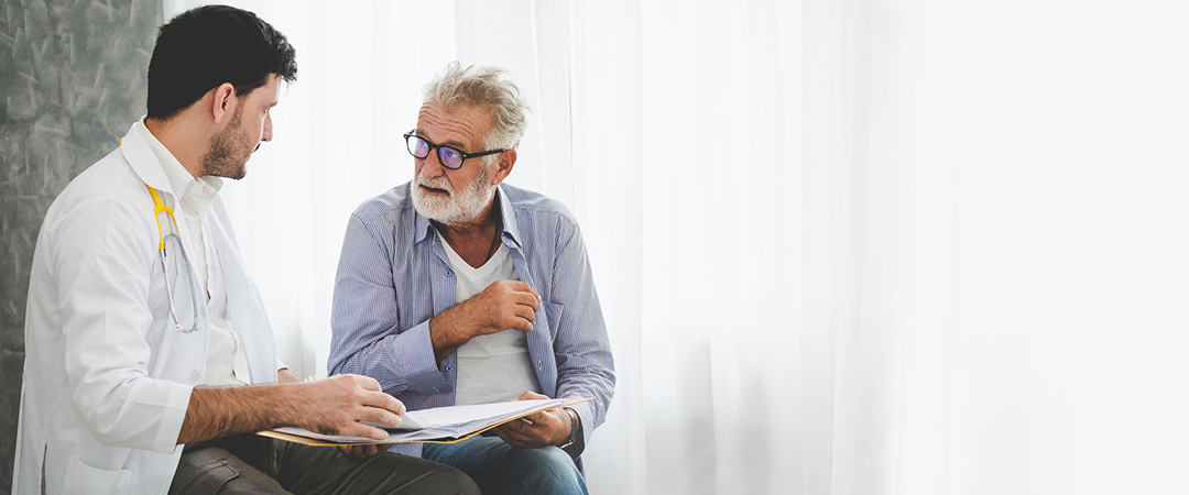 Older man with gray beard talking to a healthcare worker with a clipboard
