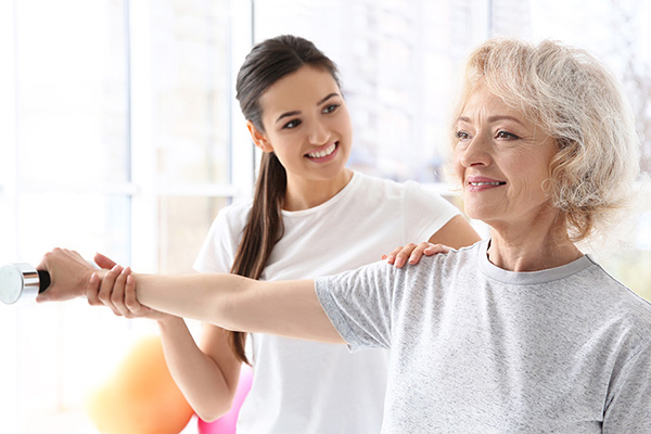 A senior and a rehab specialist helping the senior lifts weights safely.