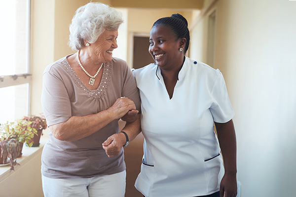 A senior and a healthcare worker walking arm-in-arm down a hallway.