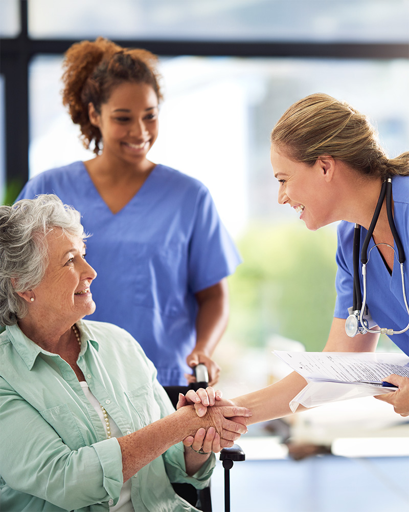 Two healthcare workers shaking hands with a senior woman.