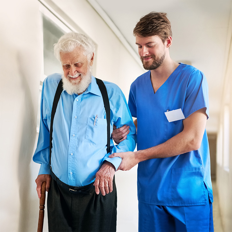 Healthcare worker helping a senior man with white beard and cane to walk.