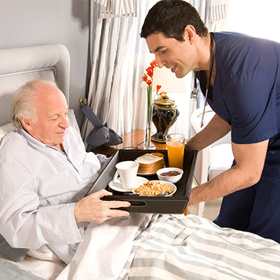 A senior being served food in his bed.