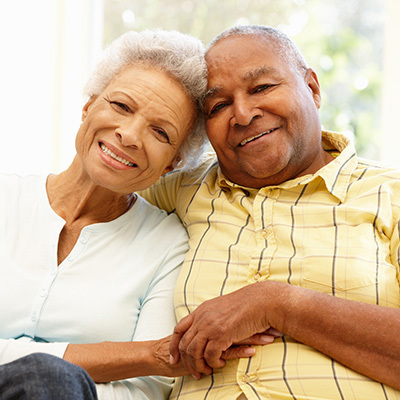 A senior couple holding hands while they are sitting together smiling.