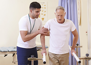 Physical therapist assisting an elderly gentleman using parallel bars for walking support