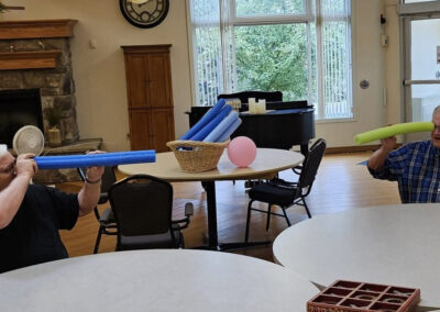 Two elderly men playing I spy with pool noodles at Elm Crest