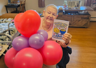 An older woman holding a card and balloons at Elm Crest