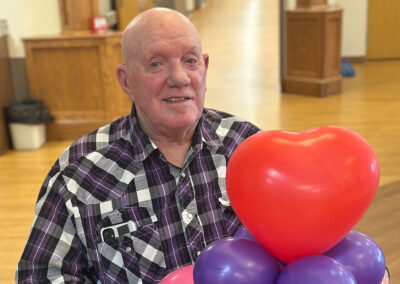 An older man holding a card and balloons at Elm Crest