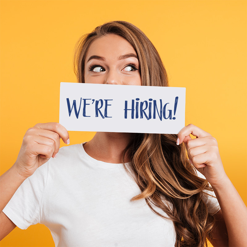 Woman with long brown hair holding a "we're hiring" sign