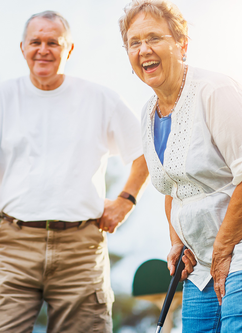 elderly couple outside laughing and golfing together