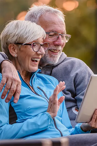Senior man and woman smiling looking at an ipad.
