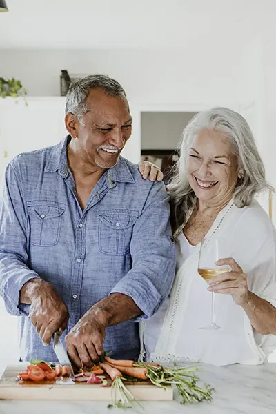 Senior man and woman in a white kitchen cutting carrots and smiling.