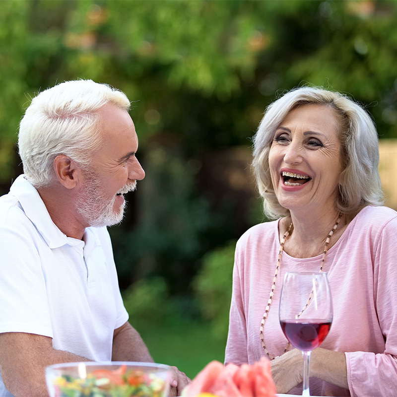 A mature couple outside eating a meal with a glass of wine.