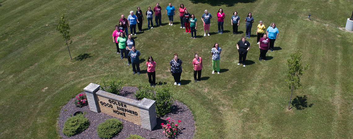 Staff on the grass outside standing in the shape of a heart with an aerial view
