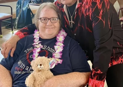 Woman in wheelchair with lei and holding a teddy bear next to an Elvis impersonator.