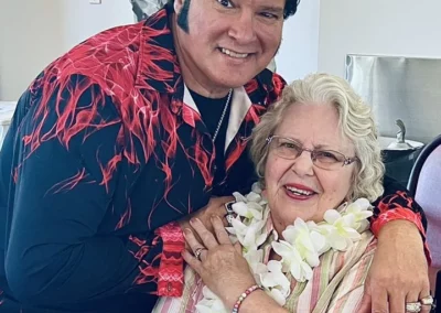 Elvis impersonator with arm around woman wearing lei and pink shirt.