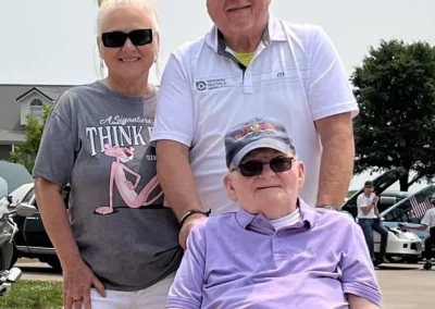 Woman and a man pushing man in purple shirt in wheelchair.
