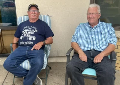 Two men outside sitting next to each other and wearing blue shirts.