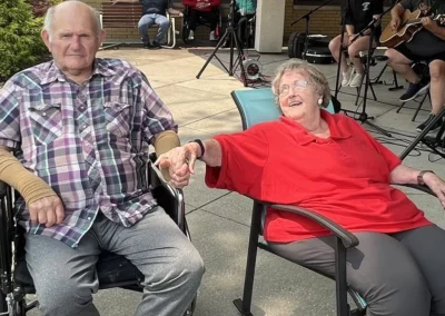 Older man in wheelchair holding hand of woman in red shirt