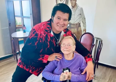 An Elvis impersonator with Vi seated, both smiling