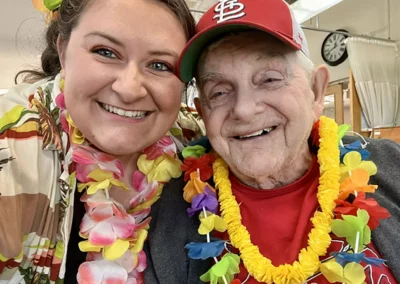 A staff member and resident taking a selfie, both wearing colorful leis