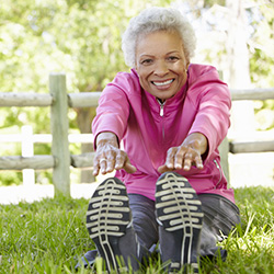 A senior in tall grass stretching her hands to her feet.