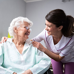 A nurse leaning in and smiling at a senior in a wheelchair.