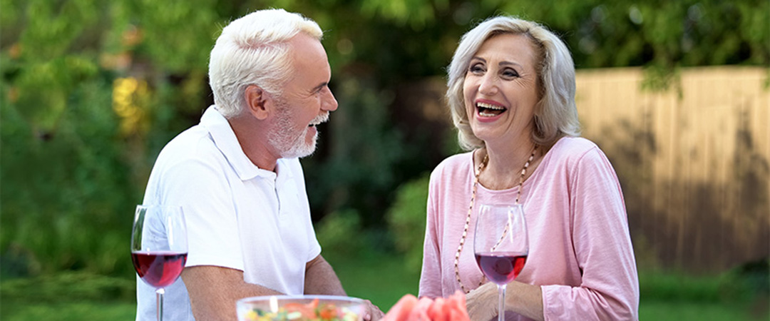 Two seniors outside dining together with a glass of wine.
