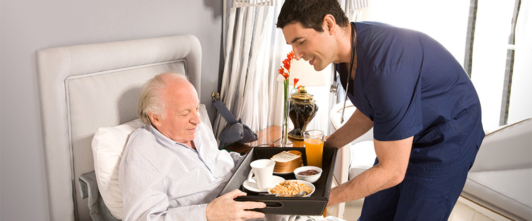 A male delivering food to a senior lying in bed.