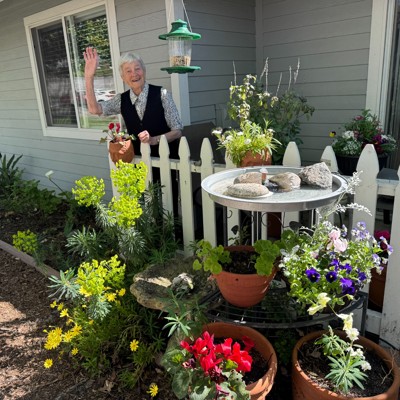 Resident next to her garden with a picket fence and waving.