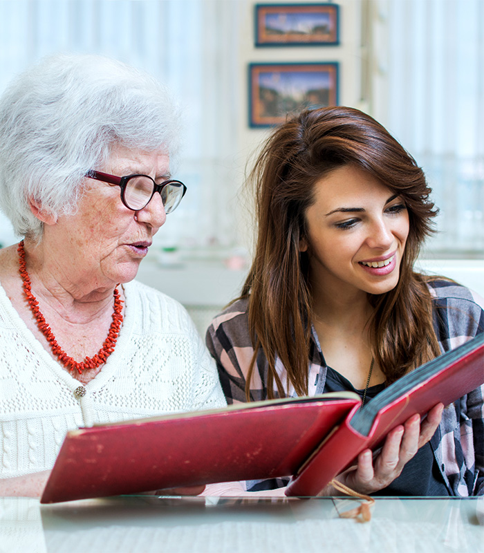 Young woman looking through scrapbook with senior woman.