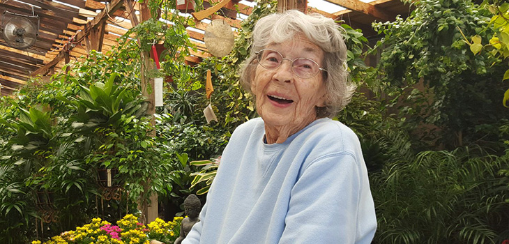 A resident in a greenhouse smiling participating in an acitivity.