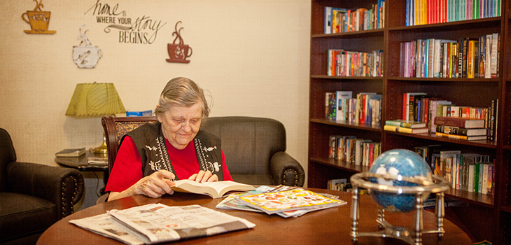 A resident in the library enjoying a good read at the table.